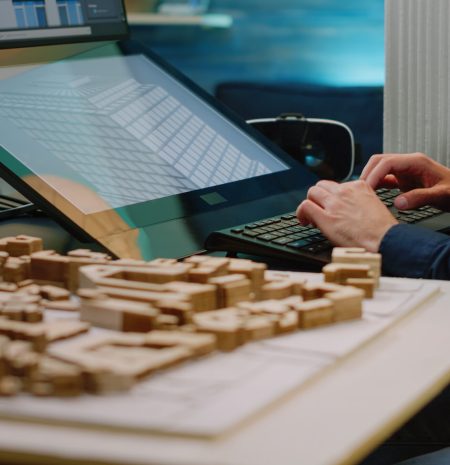 Close up of architect hands using touch screen computer and maquette on table. Man engineer working with technology to analyze building model for construction layout and development